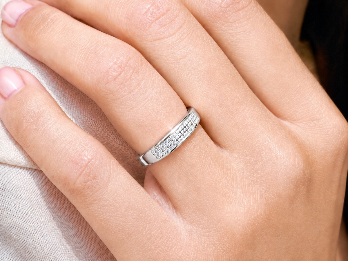 Alliance de mariage en or blanc 18 carats avec pavage 3 rangs de diamants portée au doigt d'une femme au soleil.