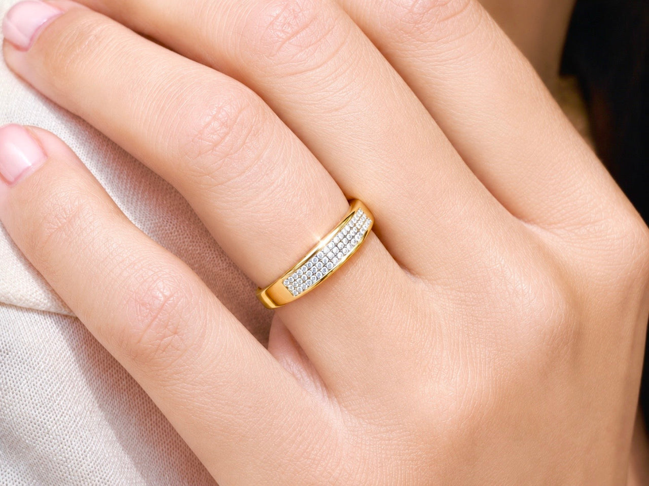 Alliance de mariage en or jaune 18 carats avec pavage 3 rangs de diamants portée au doigt d'une femme au soleil.