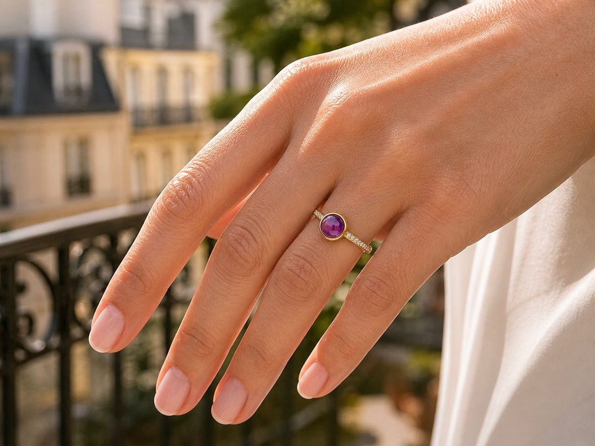 Gros plan sur une main de femme portant une bague solitaire moderne en or jaune 18 carats sertie d'une améthyste cabochon et de diamants étincelants.