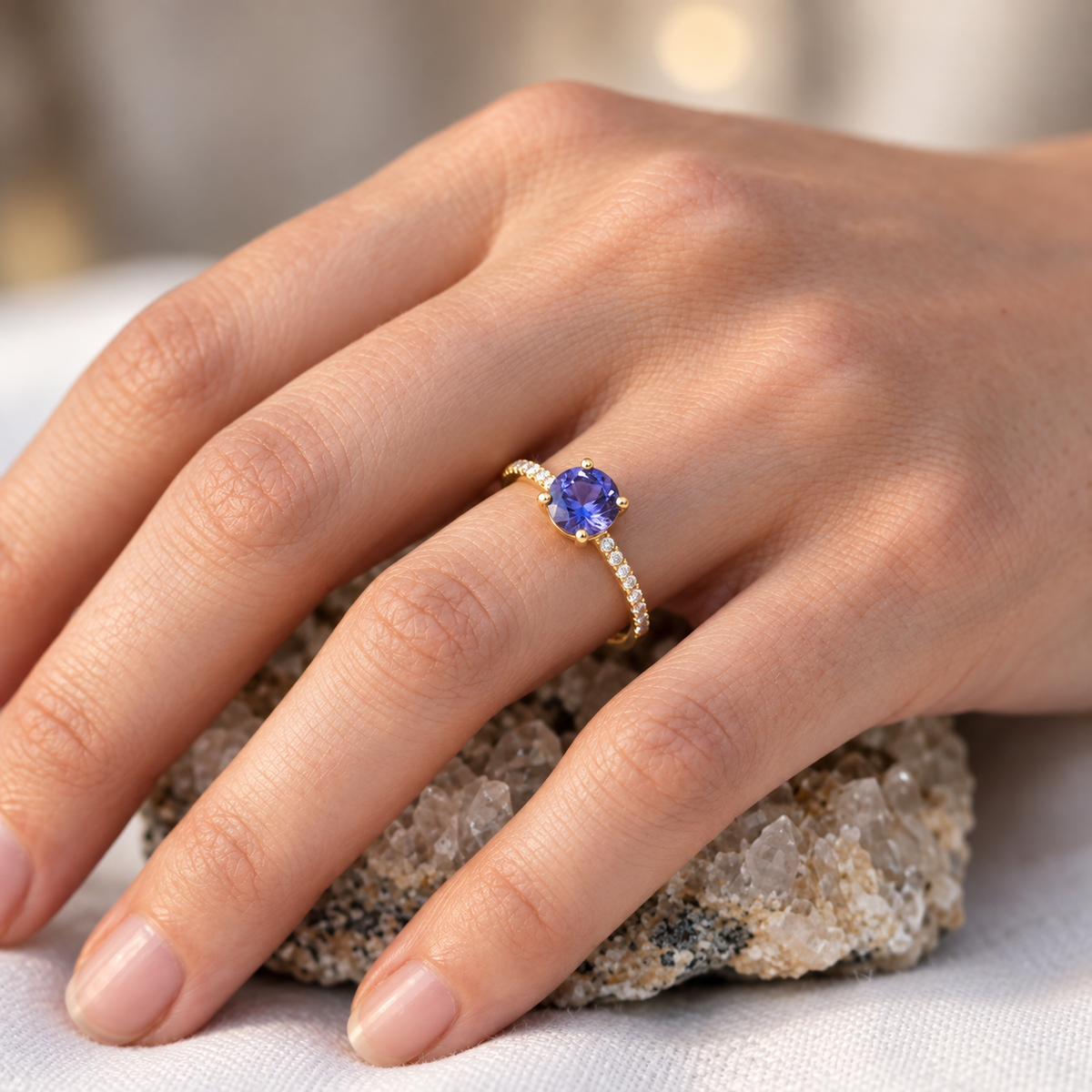 Bague de fiançailles tanzanite véritable et diamants en or jaune 18 carats portée à l'annulaire d'une femme au soleil.
