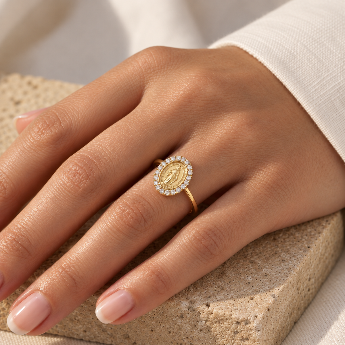 Bague Sainte Vierge en or jaune 18 carats entourée de zirconiums portée au doigt sous une lumière solaire chaude.