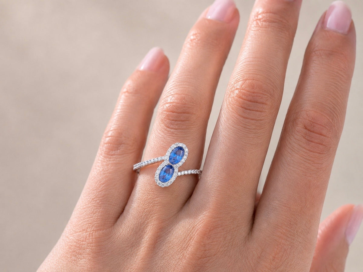 Gros plan sur une main de femme portant une bague Toi et Moi moderne en or blanc 18 carats, sertie de deux saphirs bleus et de diamants étincelants.