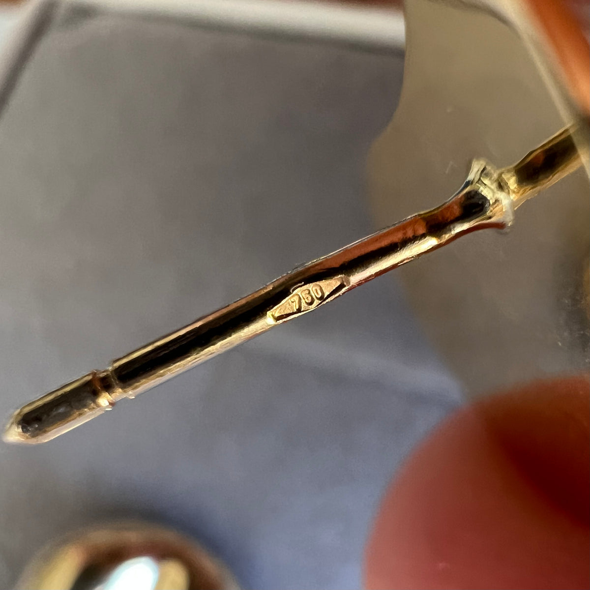 Gros plan du poinçon officiel 750 gravé sur la tige de la boucle d'oreille goutte, garantissant l'authenticité de l'or 18 carats.
