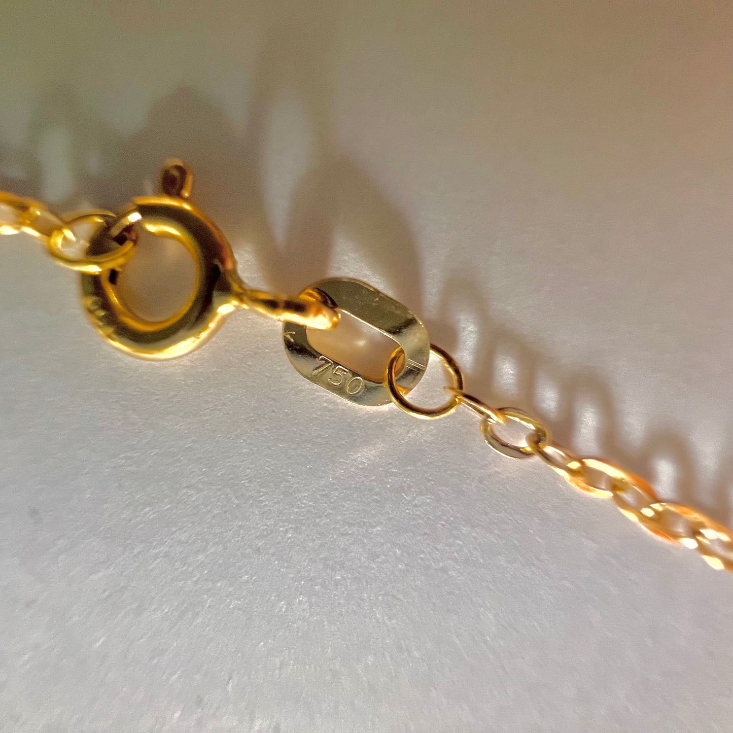 Gros plan du poinçon officiel 750 garantissant l'or jaune 18 carats sur l'attache du fermoir ressort de la chaîne homme.