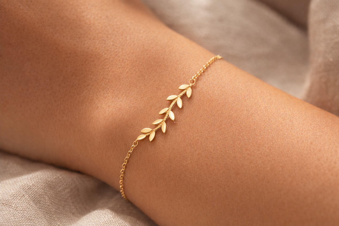 Gros plan sur un poignet de femme portant un bracelet fin en or jaune 18 carats avec un délicat motif de branche de laurier.