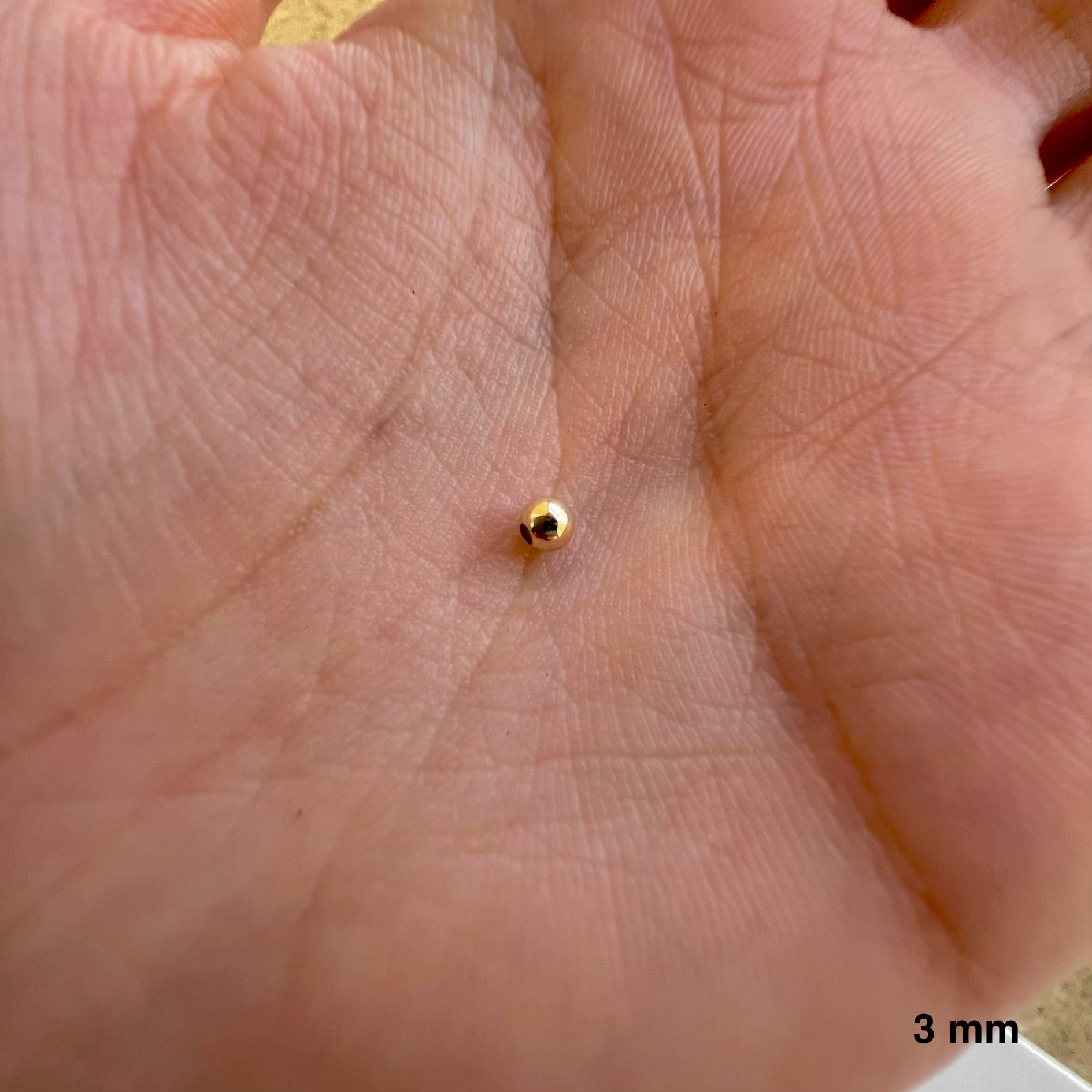 Petite perle en or 9k (375/1000) de 3 mm de diamètre au creux de la main
