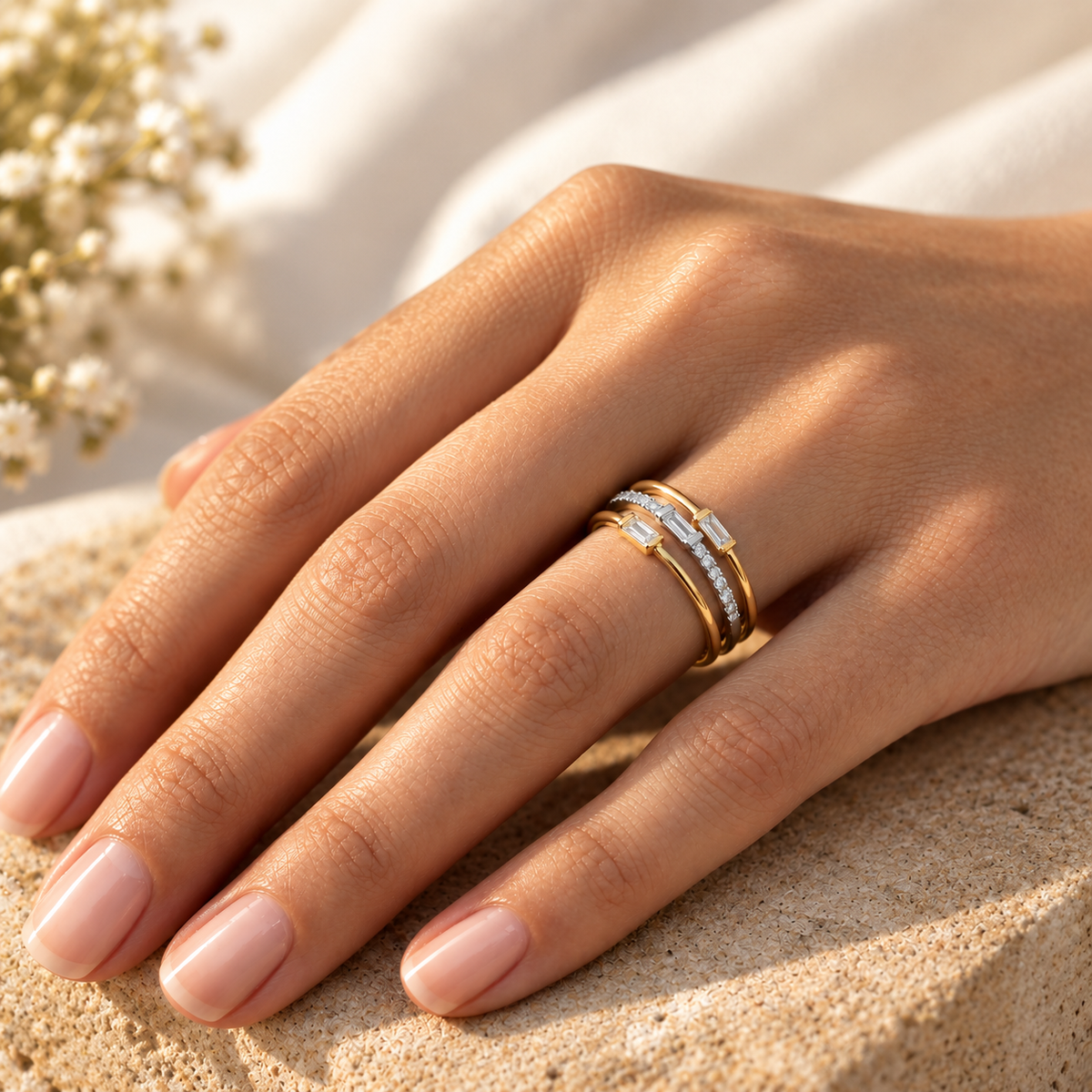 Bague bicolore 3 anneaux en or 18 carats et diamants taille baguette portée à l'annulaire d'une femme au soleil.