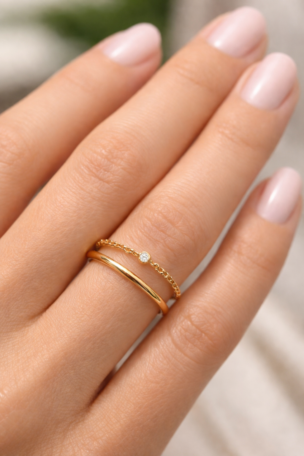Gros plan sur une main de femme portant une bague chaîne en or 18 carats sertie d'un diamant solitaire, style bijou de peau minimaliste.