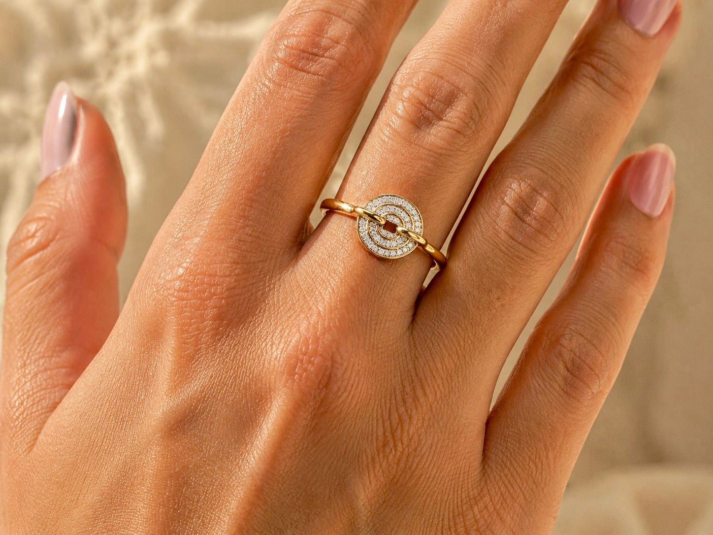Gros plan sur une main de femme portant une bague disque en or jaune 18 carats avec un pavage de diamants éclatant, design moderne et original.