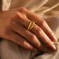Grosse bague dôme cannelée en or jaune 18 carats portée au majeur d'une femme au coucher du soleil.