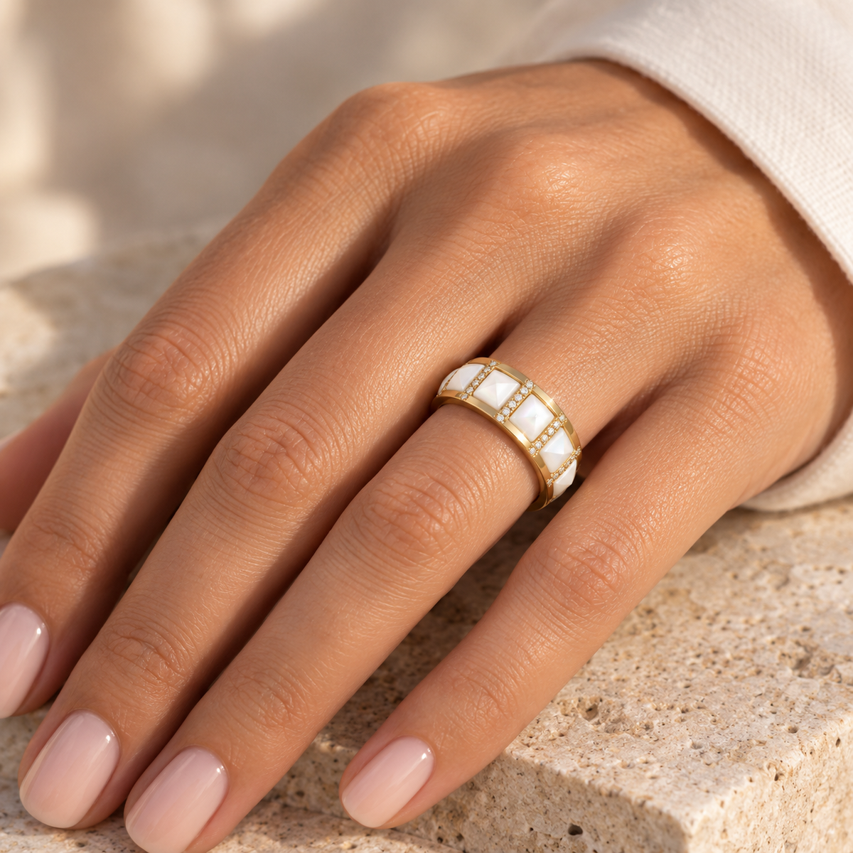 Bague Art Déco avec motif clou en nacre blanche et diamants en or jaune 18 carats portée à l'annulaire d'une femme au soleil.