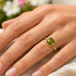 Gros plan sur une main de femme portant une bague en or jaune 18 carats sertie d'un péridot véritable taille cabochon coussin, éclat solaire et naturel.