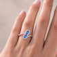 Gros plan sur une main de femme portant une bague Toi et Moi moderne en or blanc 18 carats, sertie de deux saphirs bleus et de diamants étincelants.