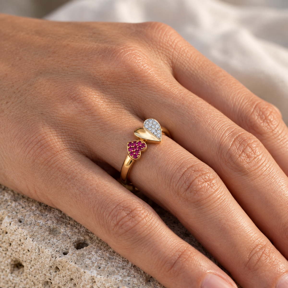 Bague coeur rubis rouge et diamants de style Toi et Moi en or jaune 18 carats, portée à l'annulaire d'une femme sous une lumière chaleureuse.