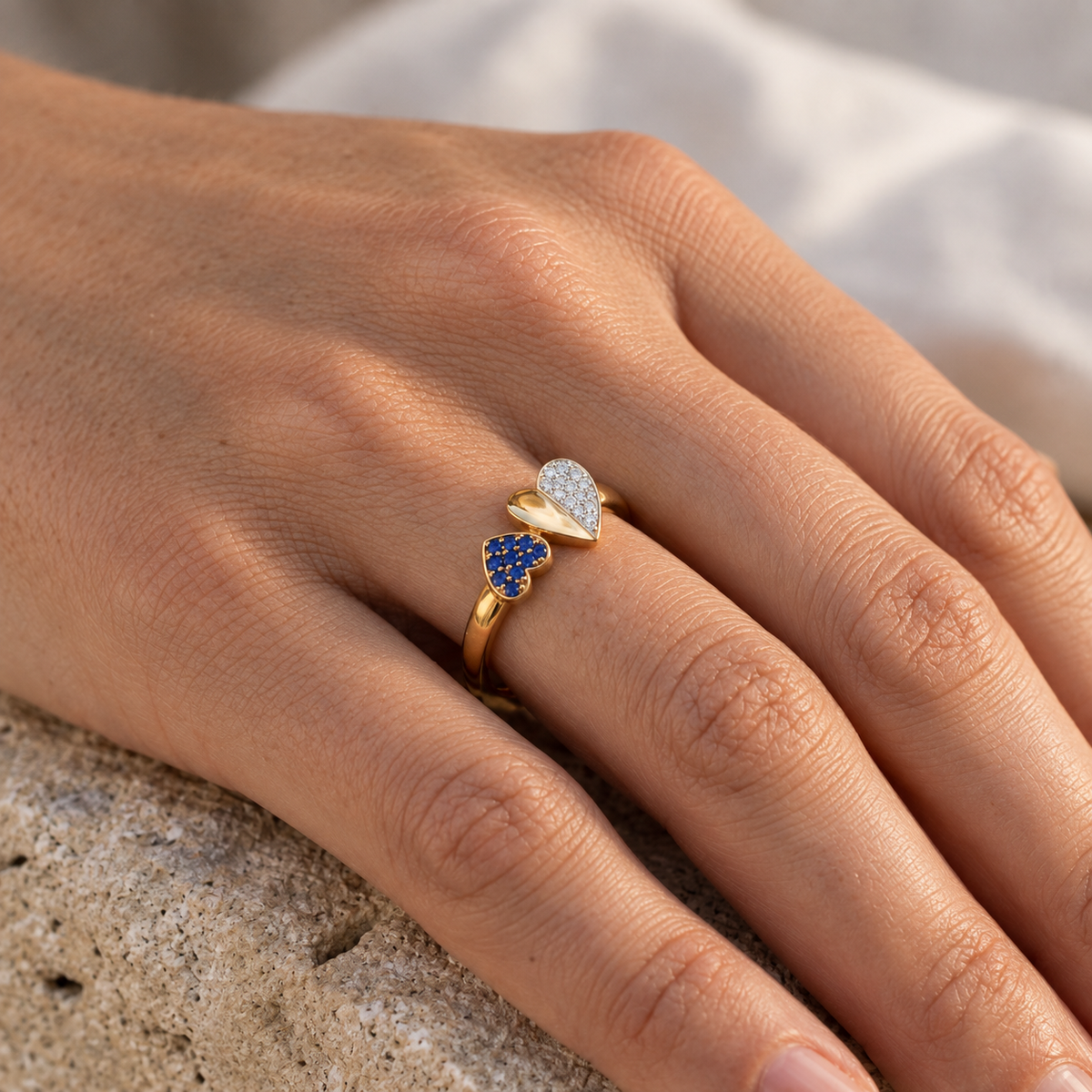 Bague de fiançailles Toi et Moi avec coeur saphir bleu et diamants en or jaune 18 carats, portée avec élégance par une femme au crépuscule.