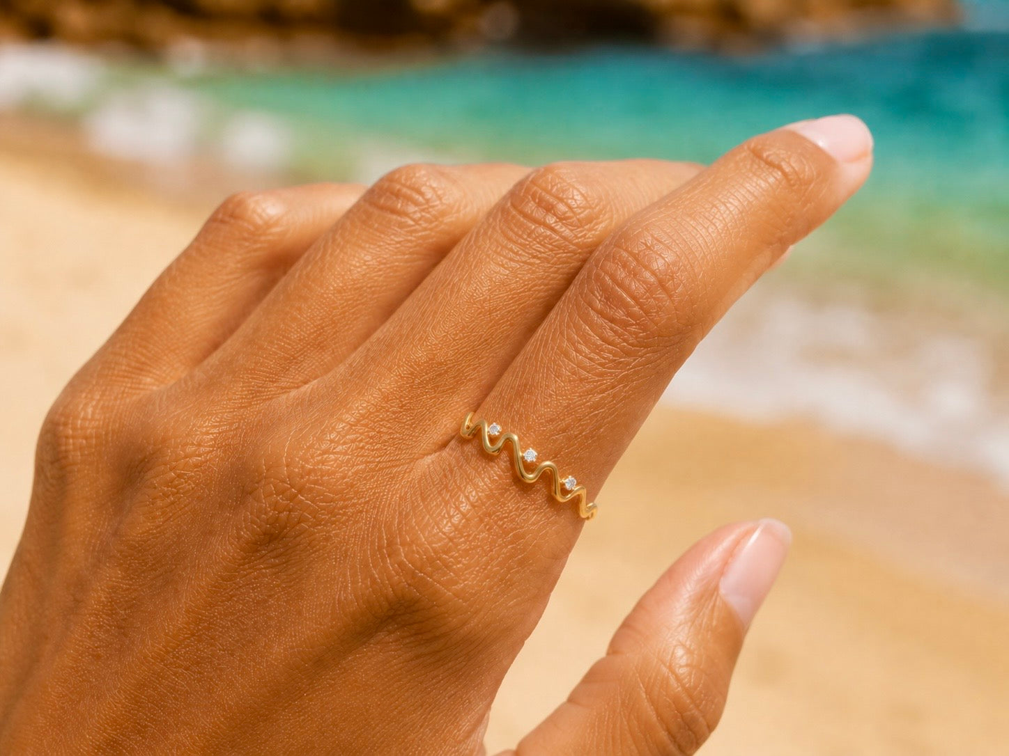 Gros plan sur une main de femme portant une bague en forme de vague en or jaune 18 carats sertie de trois diamants, portée élégamment à l'index.