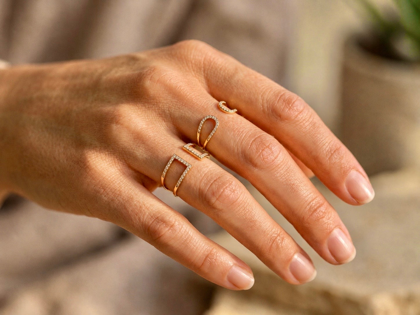 Gros plan sur une main de femme portant deux modèles de bagues ouvertes en or jaune 18 carats et diamants.