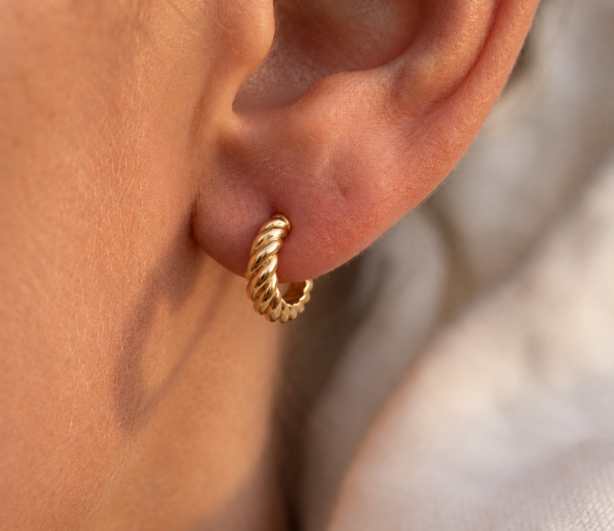Demi créole épaisse torsadée en or jaune 18 carats portée ajustée au lobe d'une femme au soleil.
