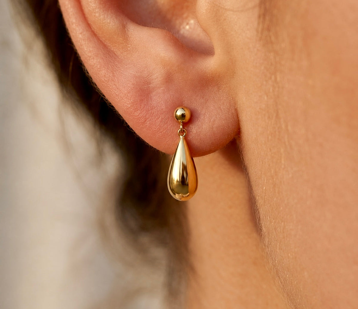 Boucle d'oreille pendante goutte en or jaune 18 carats portée par une femme au coucher du soleil.