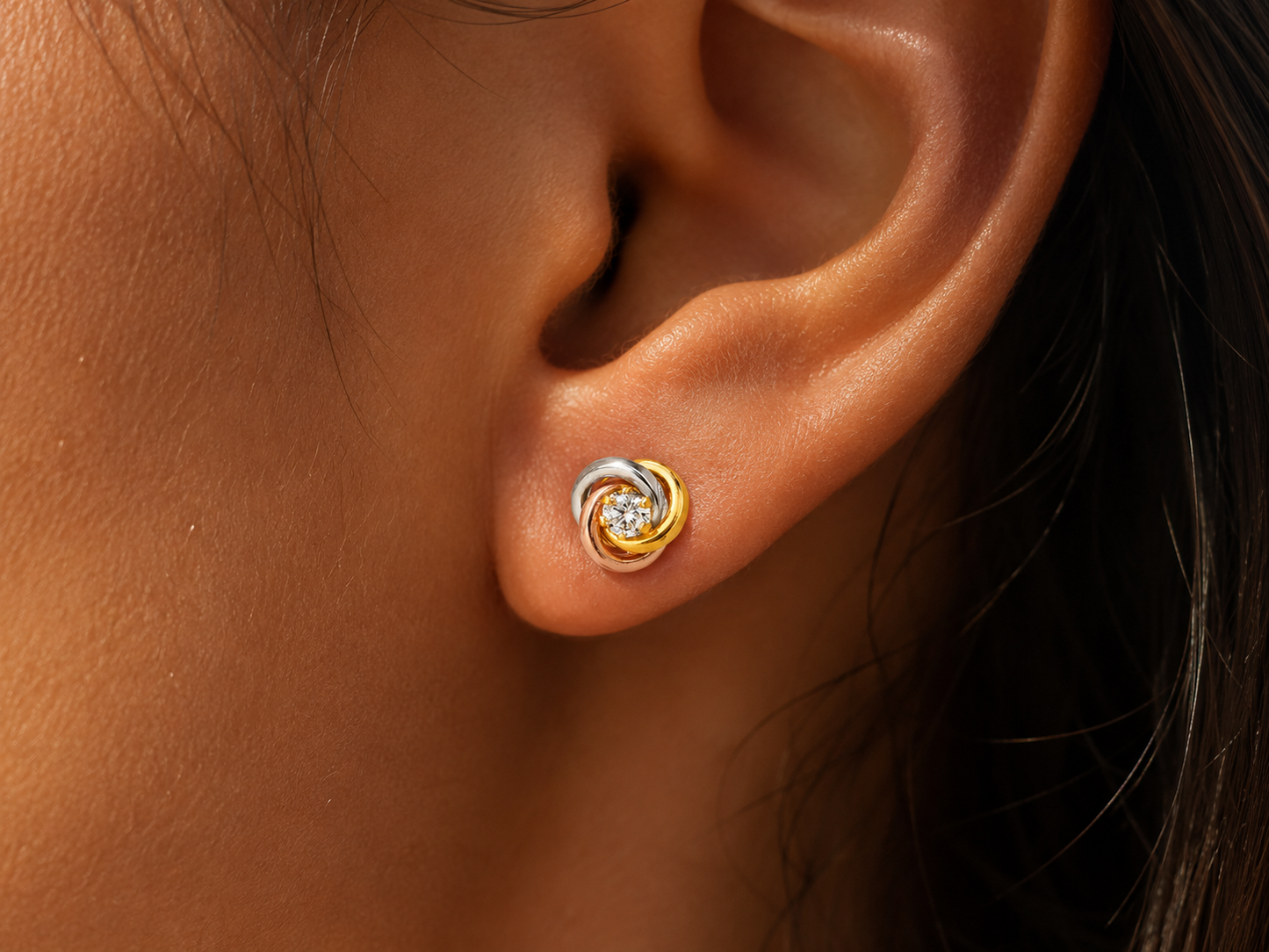 Puces d'oreilles 3 ors 18 carats en forme de nœud portées au lobe sous une lumière solaire.