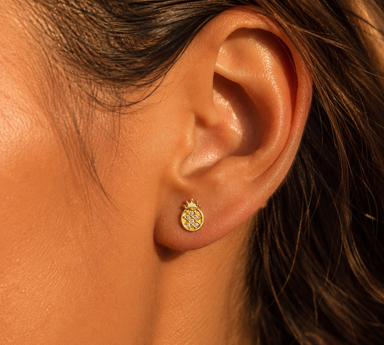 Puce d'oreille ananas en or jaune 18 carats portée au lobe d'une femme au soleil.