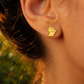 Gros plan sur une oreille de femme portant une puce d'oreille en or jaune 18 carats en forme de carte de la Guyane, bijou de 10x8 mm.