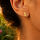 Gros plan sur une oreille de femme portant une puce d'oreille en or jaune 18 carats en forme de carte de la Martinique, bijou de 14x9 mm.