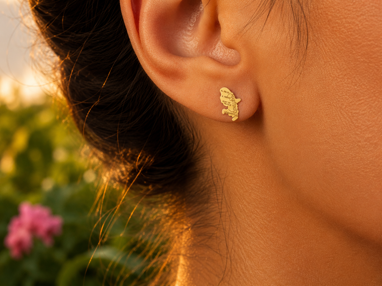 Gros plan sur une oreille de femme portant une puce d'oreille en or jaune 18 carats en forme de carte de la Martinique, bijou de 14x9 mm.