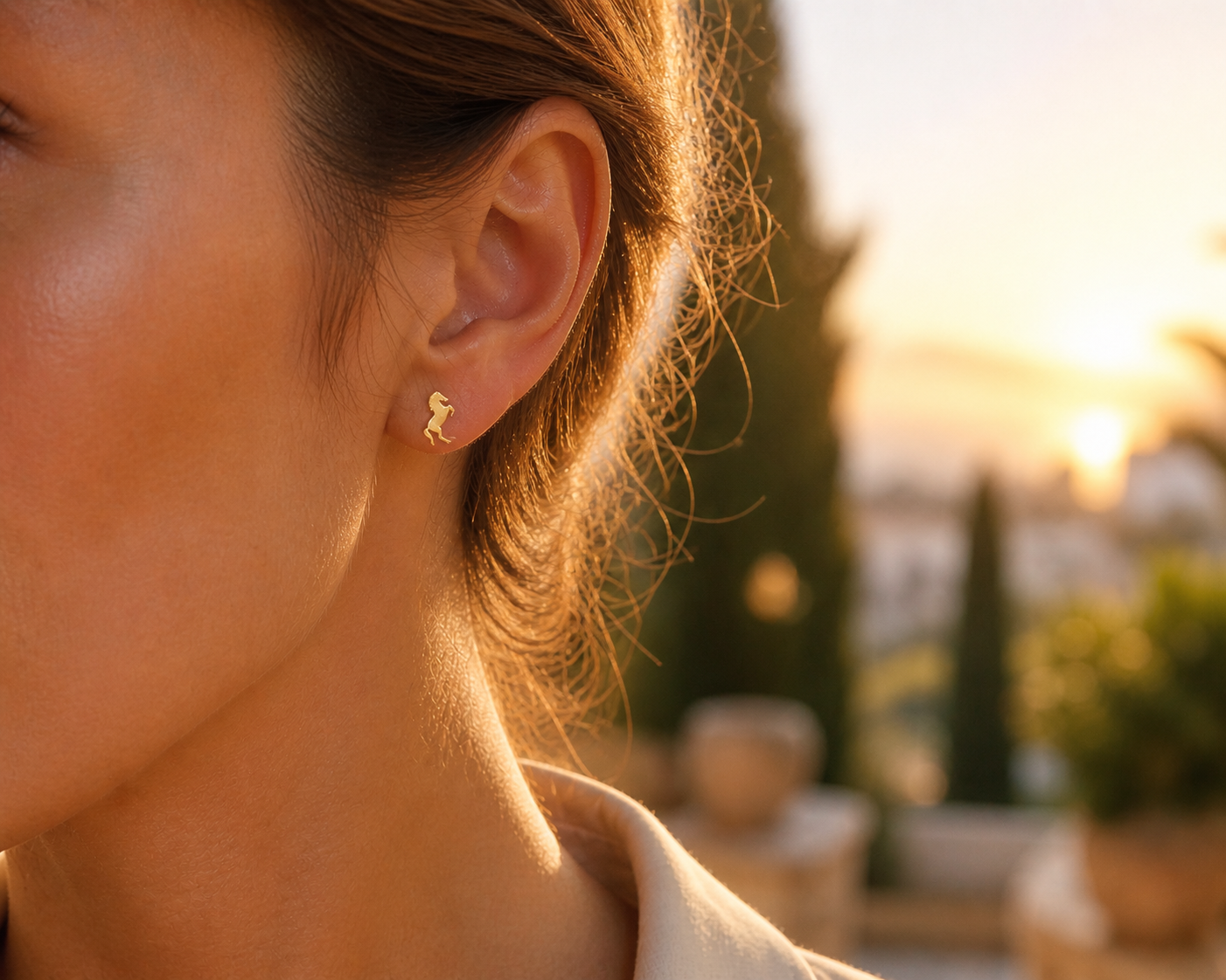 Gros plan sur une oreille de femme portant de petites puces d'oreilles cheval cabré en or jaune 18 carats