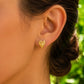 Gros plan sur une oreille de femme portant des boucles d'oreilles en forme de feuille d'Anthurium en or jaune 18 carats, un bijou botanique élégant et lumineux.