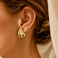 Boucle d'oreille goutte d'eau bombée en or jaune 18 carats portée ajustée au lobe d'une femme au coucher du soleil.
