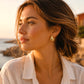 Boucles d'oreilles gouttes d'eau en or jaune 18 carats portées par une femme de profil habillée de blanc au crépuscule.