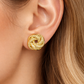 Paire de boucles d'oreilles nœud antillais en or jaune 14 carats, entrelacement de fils lisses et ciselés, diamètre 13mm portees par une femme