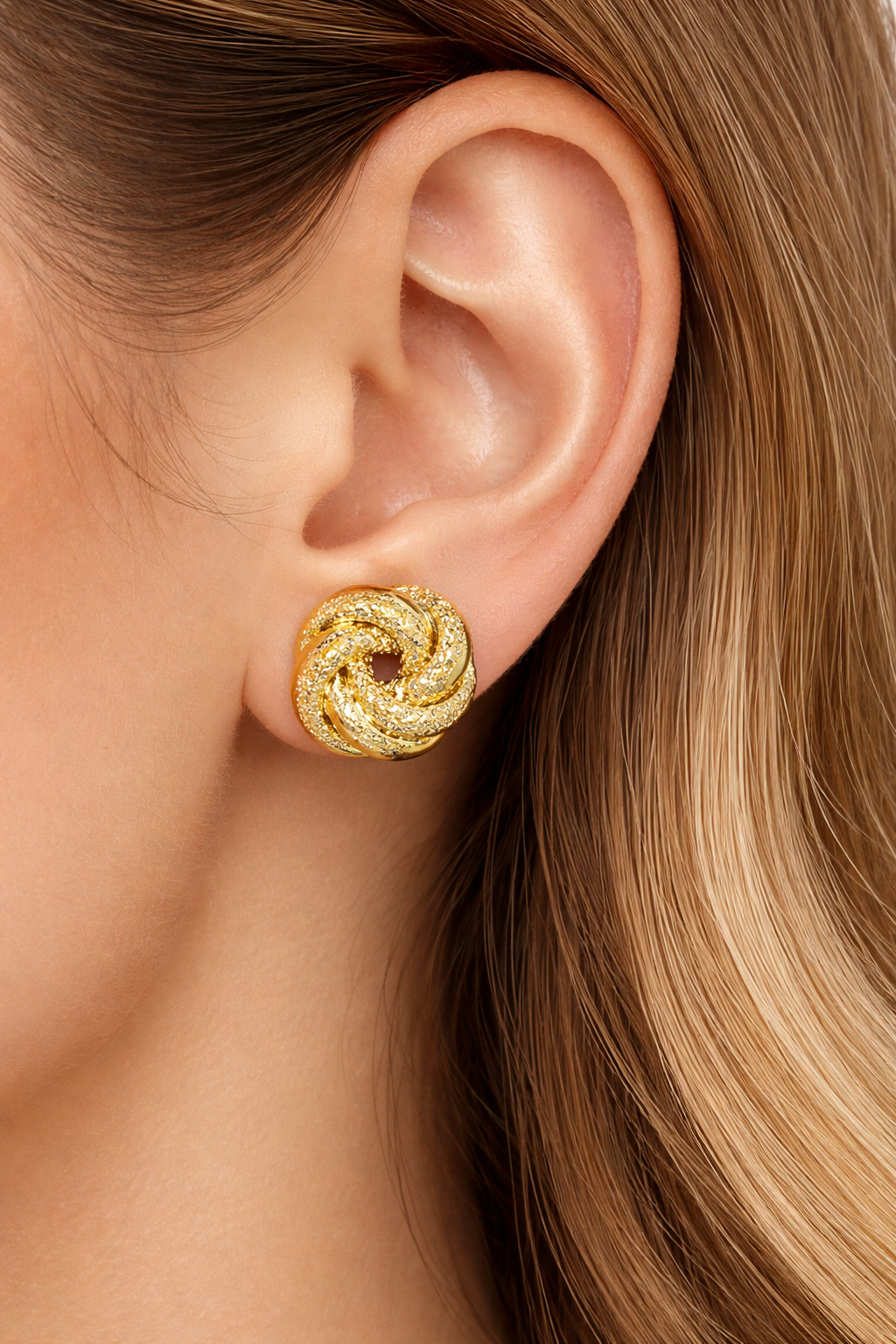Paire de boucles d'oreilles nœud antillais en or jaune 14 carats, entrelacement de fils lisses et ciselés, diamètre 13mm portees par une femme