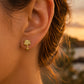 Gros plan sur une oreille de femme portant une puce d'oreille en forme de palmier en or jaune 18 carats, éclat solaire et style exotique.