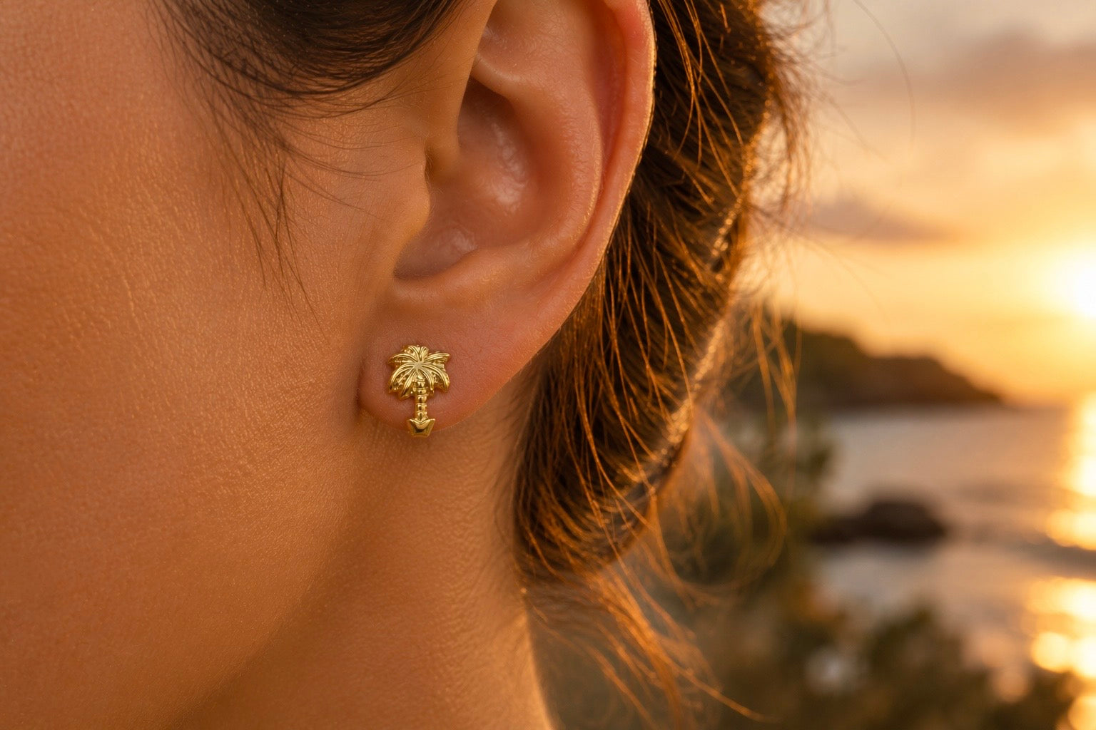 Gros plan sur une oreille de femme portant une puce d'oreille en forme de palmier en or jaune 18 carats, éclat solaire et style exotique.