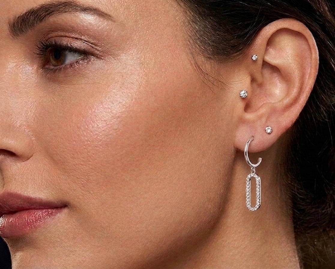 Gros plan sur une oreille de femme portant des boucles d'oreilles pendantes en or blanc 18 carats serties de diamants, motif rectangle évidé moderne.