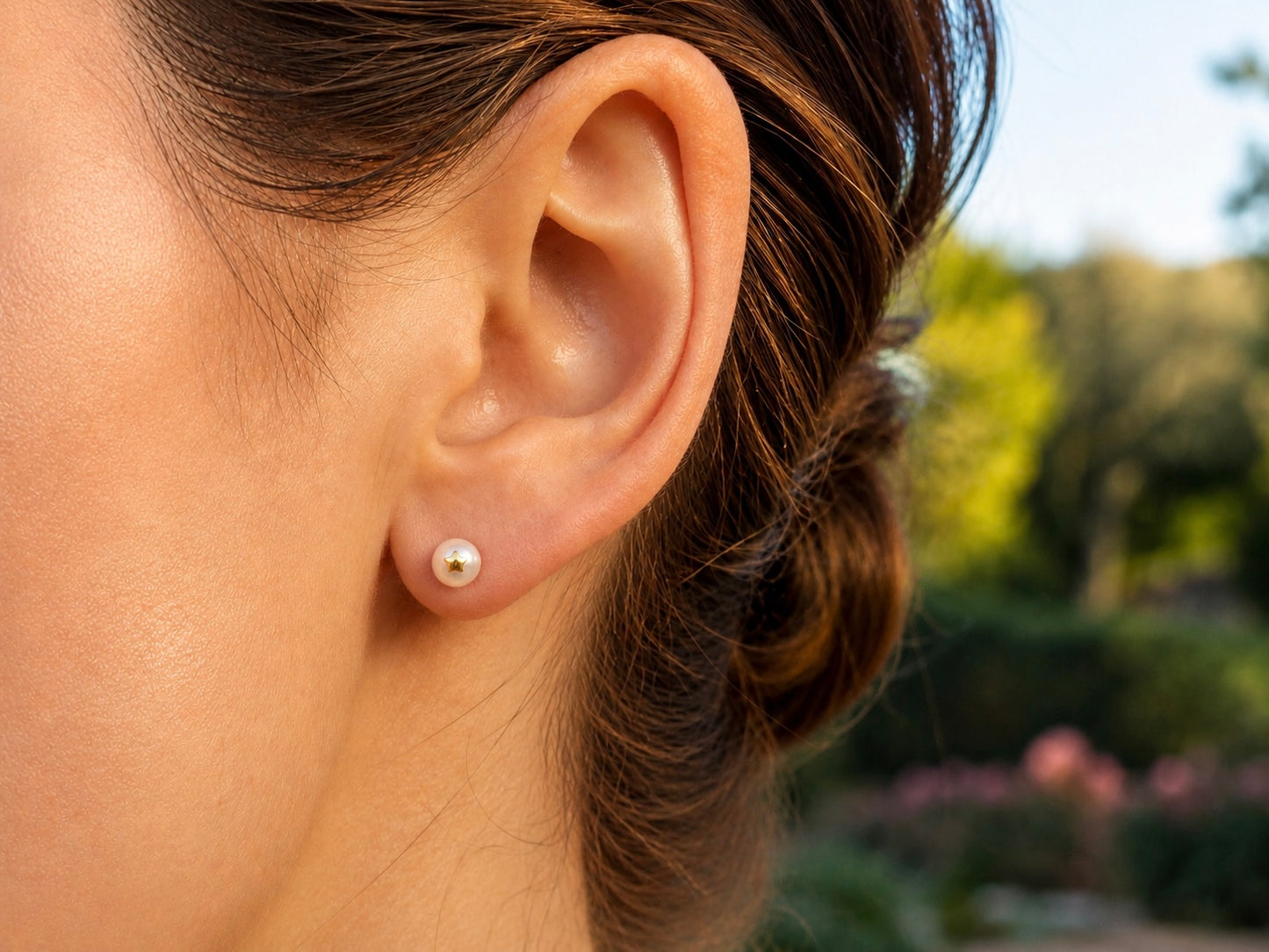 Oreille de femme portant une puce d'oreille en perle de culture ornée d'une étoile en or jaune 18 carats.