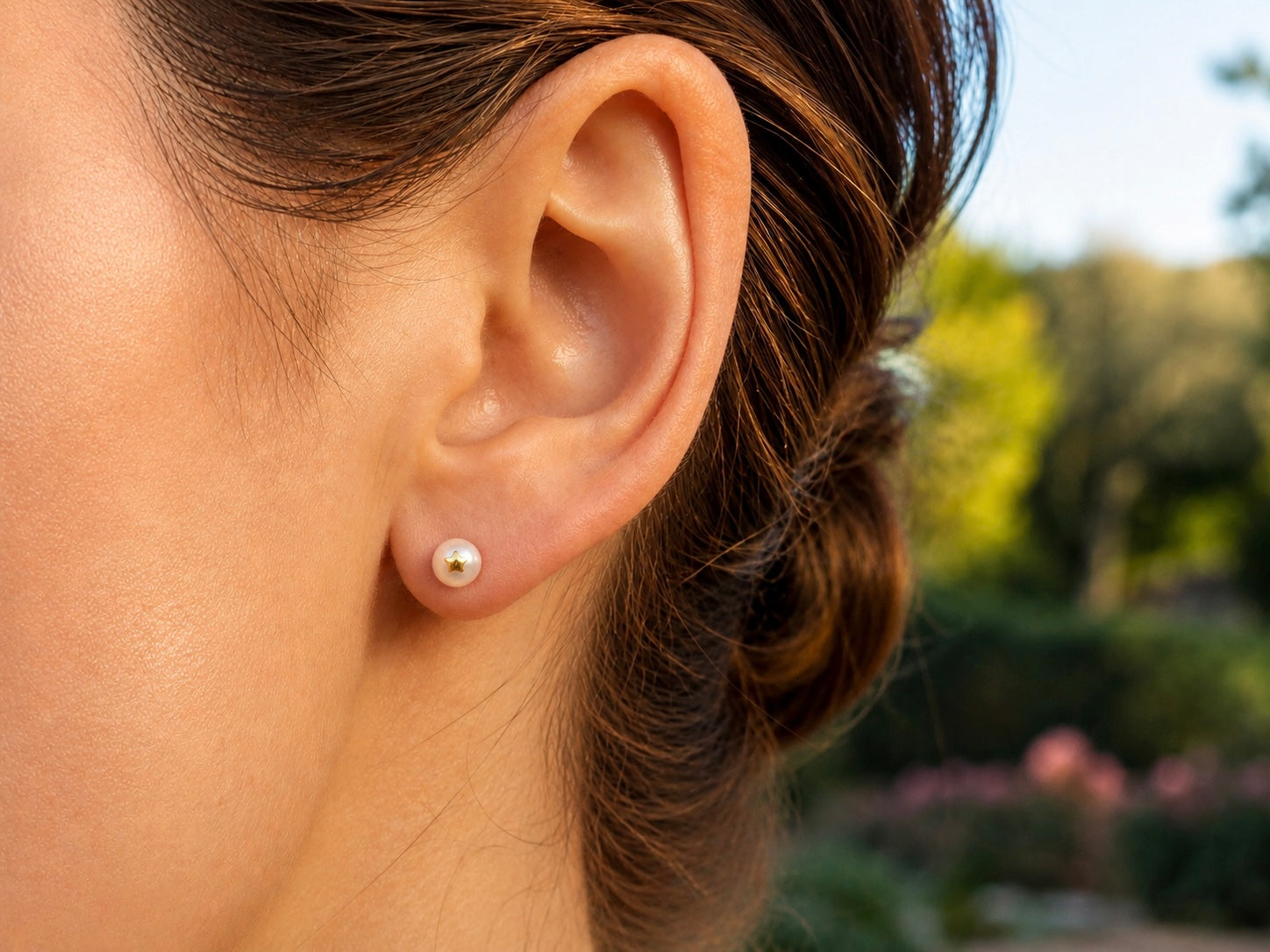 Oreille de femme portant une puce d'oreille en perle de culture ornée d'une étoile en or jaune 18 carats.