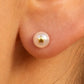 Gros plan sur une oreille de femme portant une puce d'oreille en perle de culture ornée d'une étoile en or jaune 18 carats.
