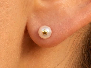 Gros plan sur une oreille de femme portant une puce d'oreille en perle de culture ornée d'une étoile en or jaune 18 carats.