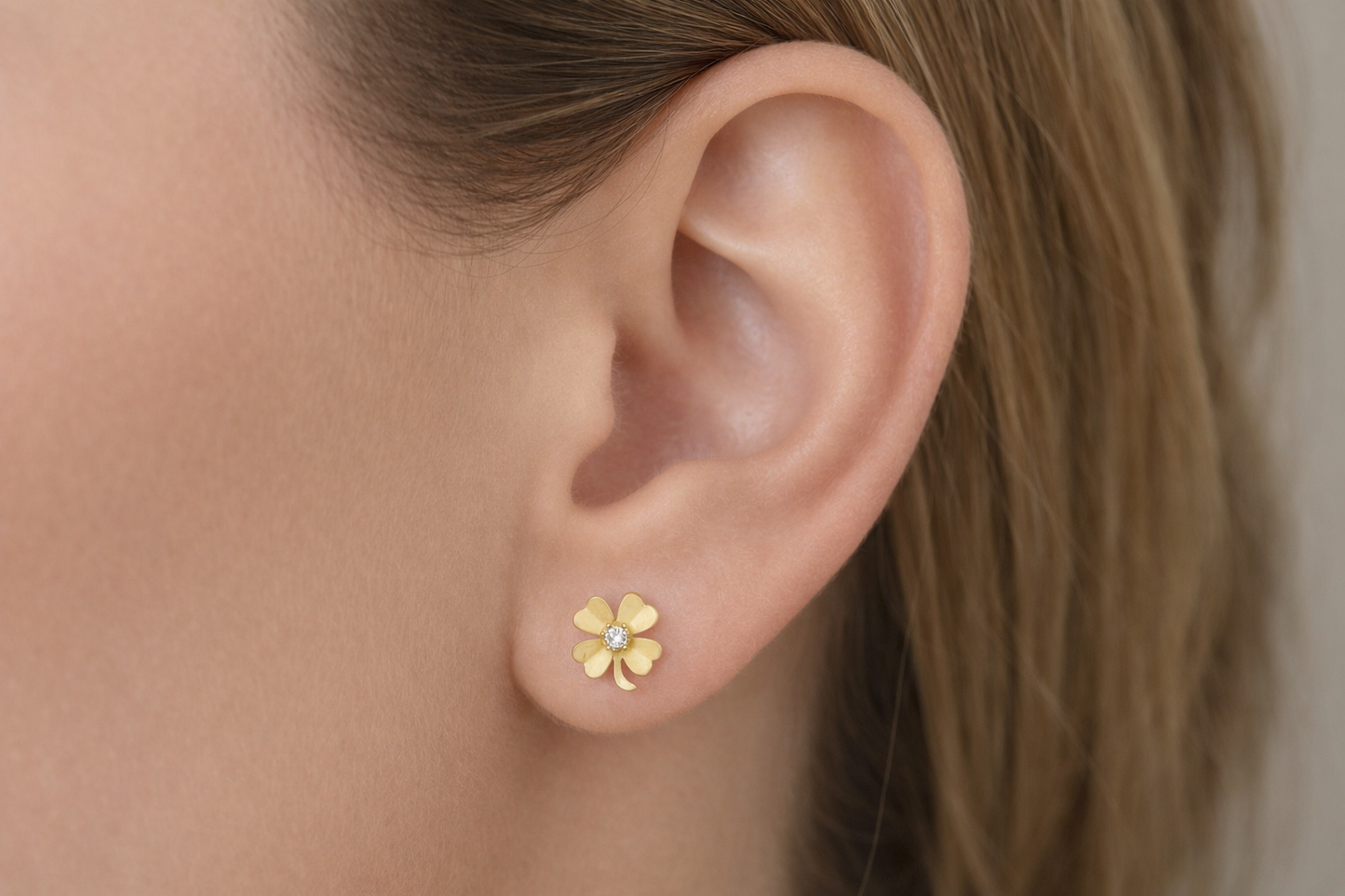 Paire de boucles d'oreilles trèfle à 4 feuilles en or jaune 18 carats avec oxyde de zirconium central portées par une femme