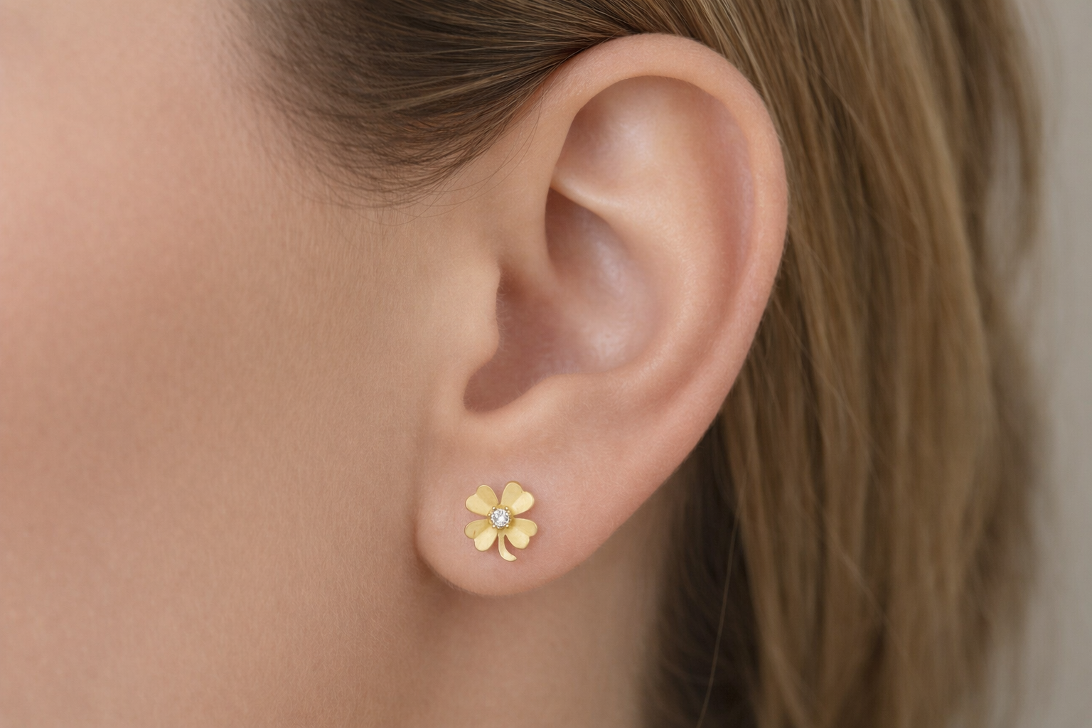 Paire de boucles d'oreilles trèfle à 4 feuilles en or jaune 18 carats avec oxyde de zirconium central portées par une femme