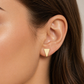  Gros plan sur une oreille de femme portant des puces d'oreilles triangle en or jaune 18 carats, design géométrique et minimaliste.