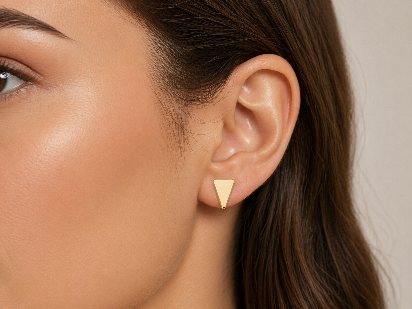  Gros plan sur une oreille de femme portant des puces d'oreilles triangle en or jaune 18 carats, design géométrique et minimaliste.