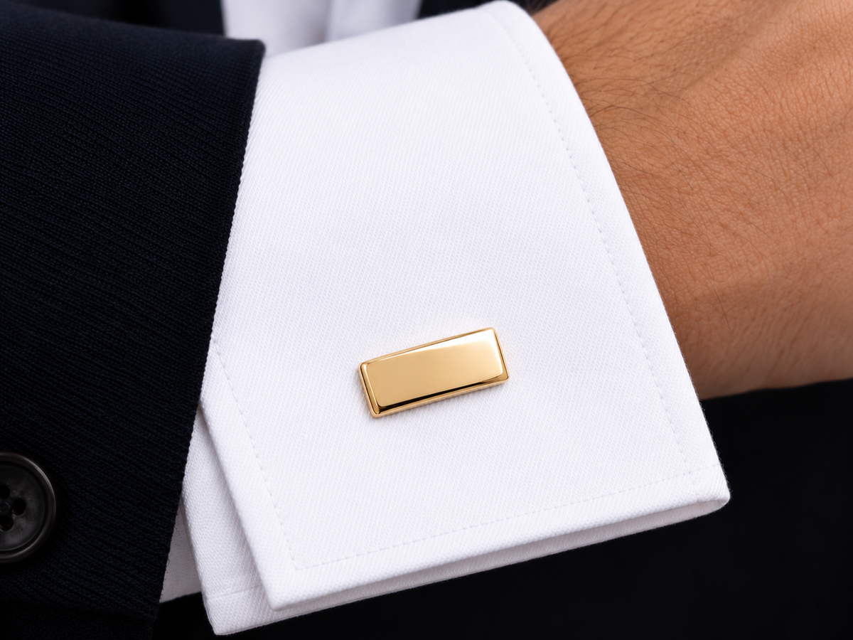 Bouton de manchette rectangulaire en or jaune 18 carats massif porté sur le poignet mousquetaire d'une chemise blanche.