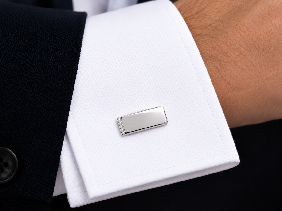 Boutons de manchette minimalistes en or blanc 18 carats portés avec élégance sur une chemise blanche sous une veste de costume.

