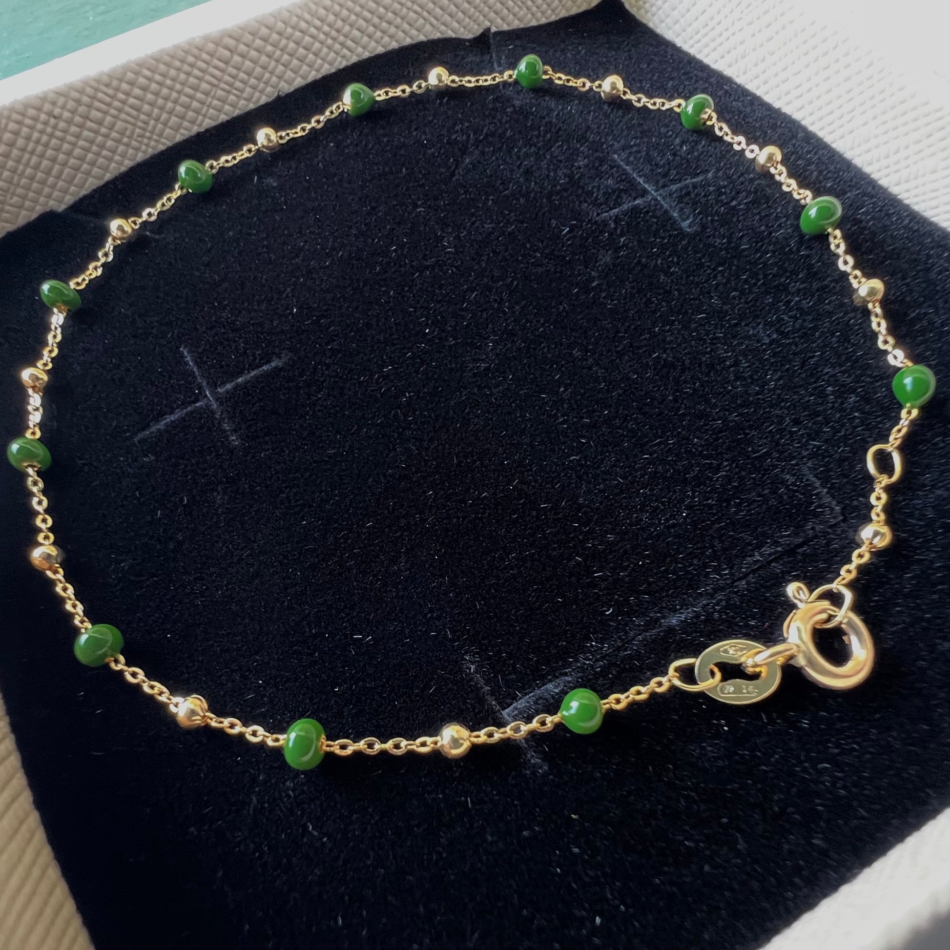 Bracelet en or jaune 18 carats avec boules d'or et résine verte sur velours, gros plan sur le fermoir ressort et le poinçon officiel 750.