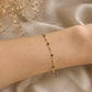 Bracelet chaîne en or jaune 18 carats alternant boules d'or et perles d'or recouvertes de résine verte, porté au poignet sur un tissu drapé beige.