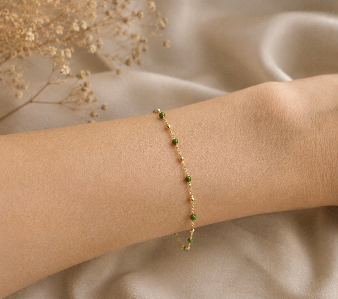 Bracelet chaîne en or jaune 18 carats alternant boules d'or et perles d'or recouvertes de résine verte, porté au poignet sur un tissu drapé beige.